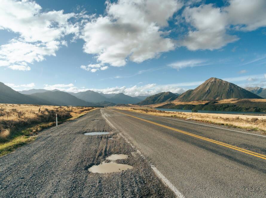 Potholes on a rural road with mountains and clear sky in the background